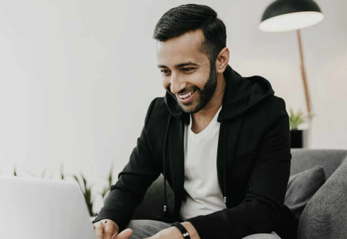 smiling man in hoodie typing on a laptop